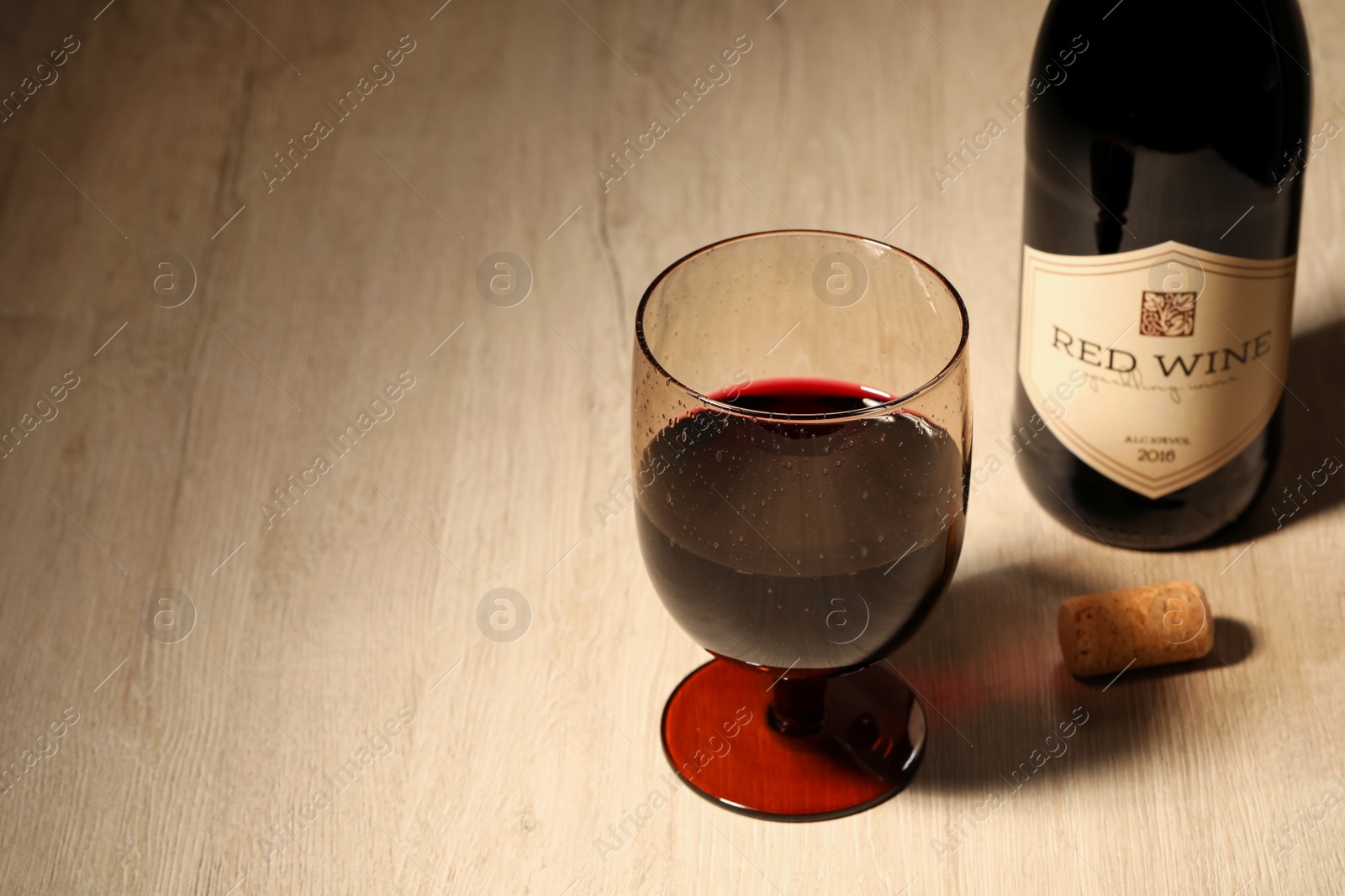 Photo of Glass of red wine near bottle on wooden table. Space for text