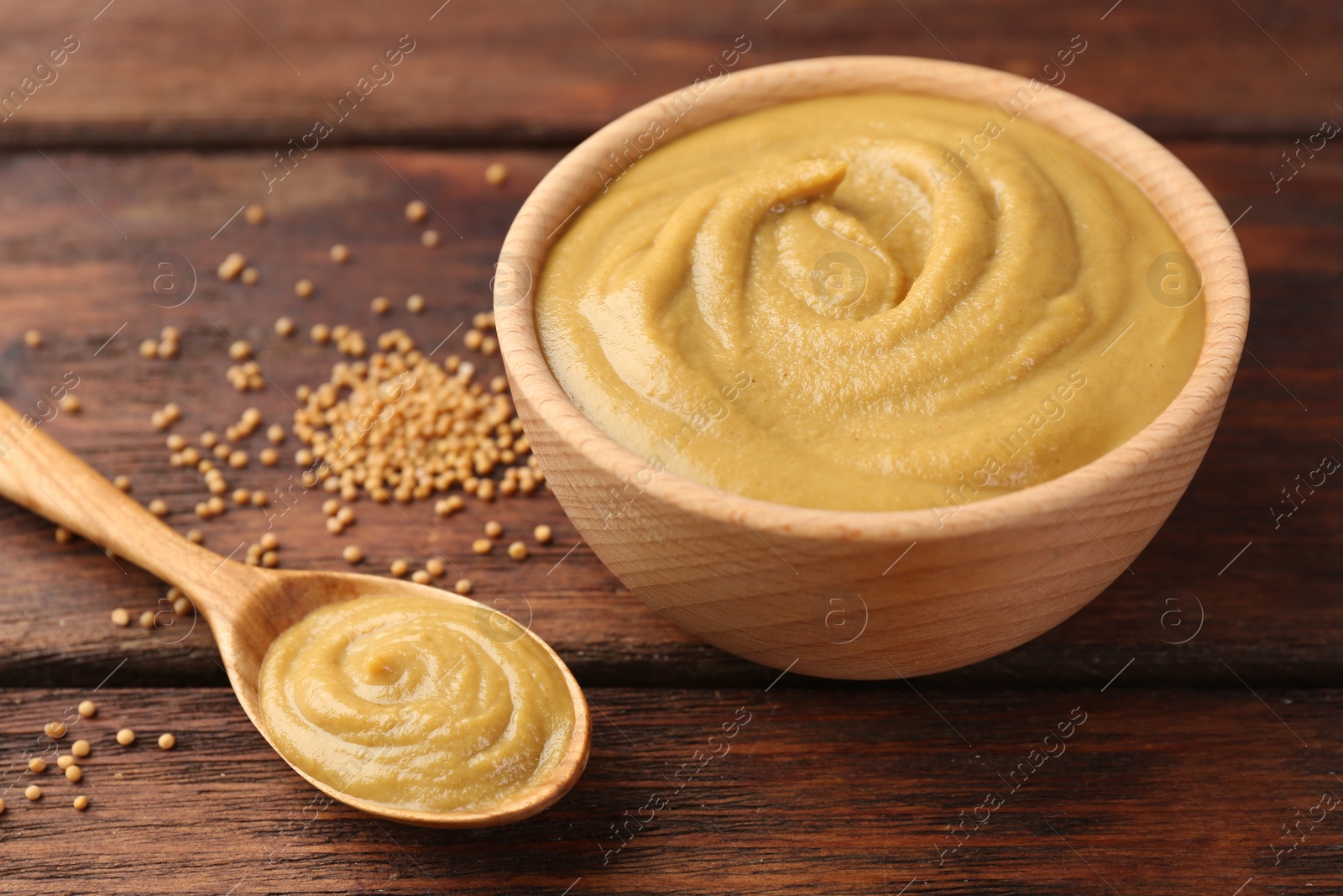 Photo of Tasty mustard sauce and dry seeds on wooden table, closeup