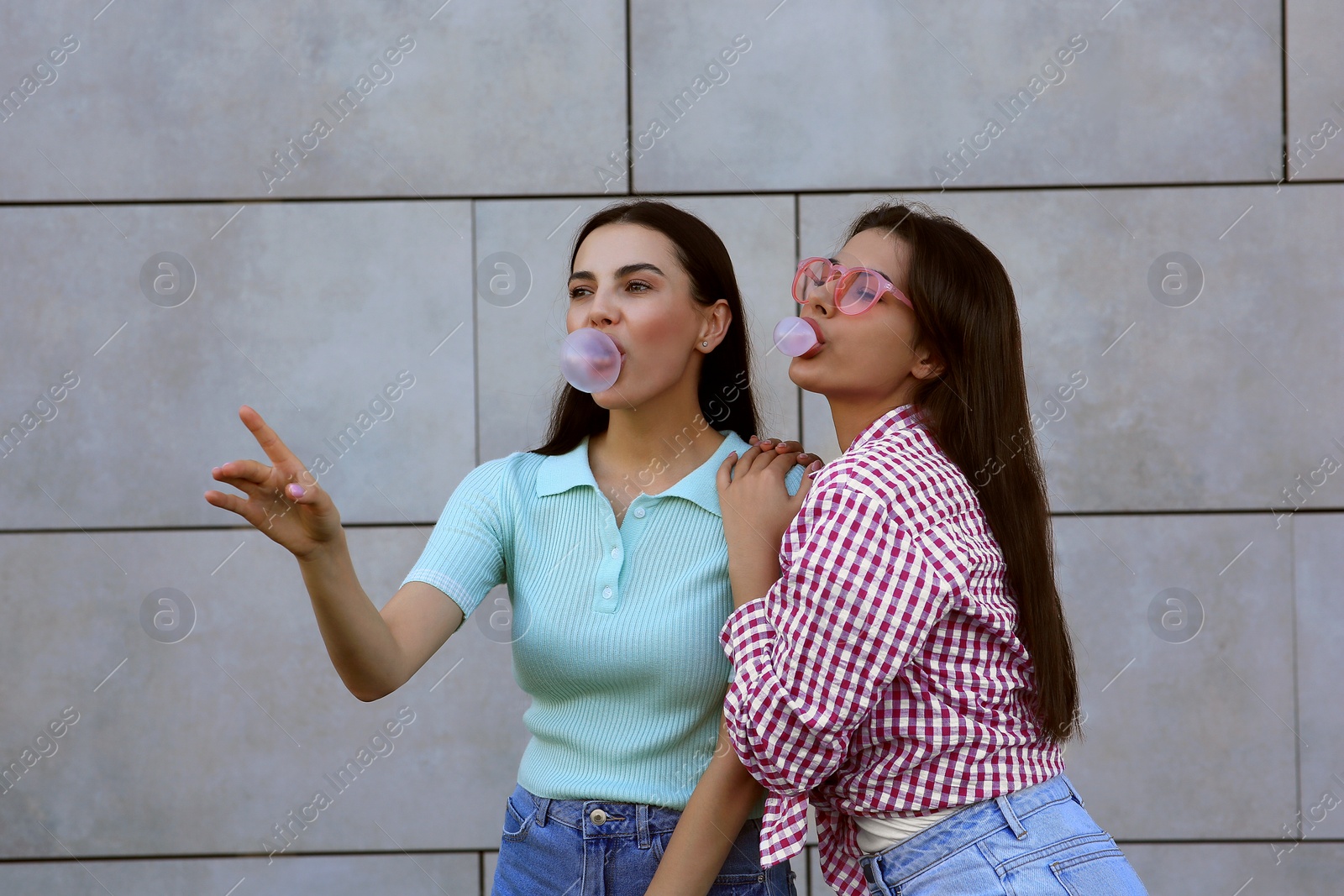 Photo of Beautiful women blowing gums near wall outdoors