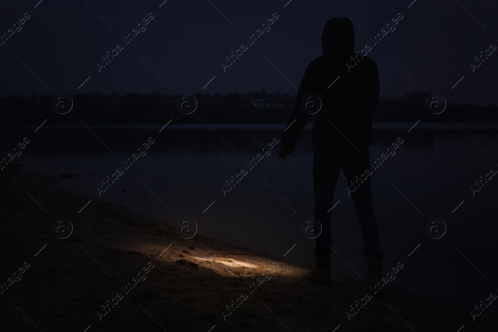 Photo of Man with flashlight walking near river at night