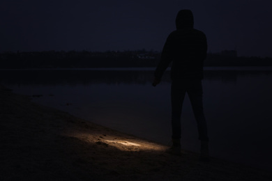 Man with flashlight walking near river at night