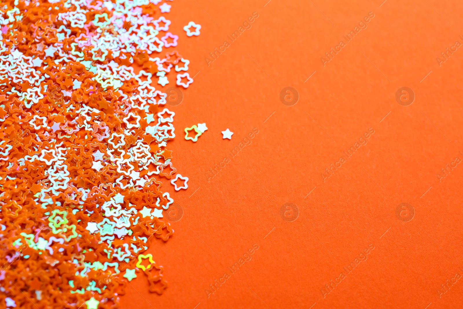 Photo of Shiny bright star shaped glitter on orange background. Space for text