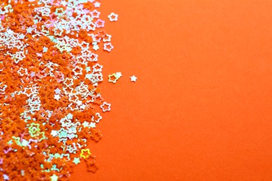 Shiny bright star shaped glitter on orange background. Space for text