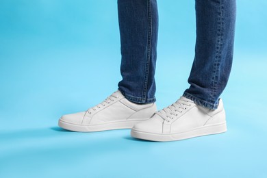 Man wearing stylish white sneakers on light blue background, closeup