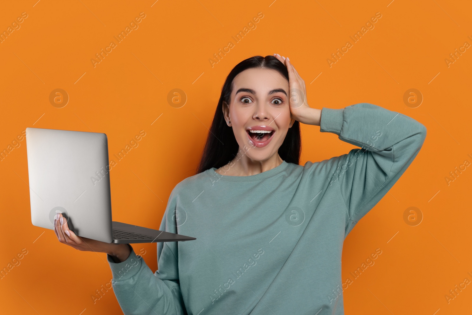 Photo of Surprised woman with laptop on orange background