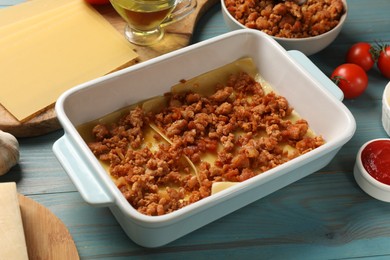 Photo of Cooking lasagna. Pasta sheets and minced meat in baking tray on light blue wooden table, closeup