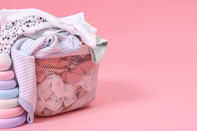 Photo of Laundry basket with baby clothes near toy on light pink background, closeup. Space for text