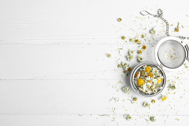 Photo of Dry chamomile flowers in infuser on white wooden table, flat lay. Space for text