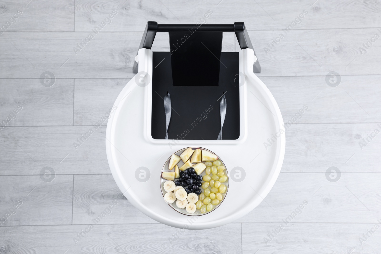 Photo of High chair with healthy baby food served on white tray indoors, top view