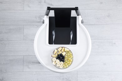 Photo of High chair with healthy baby food served on white tray indoors, top view