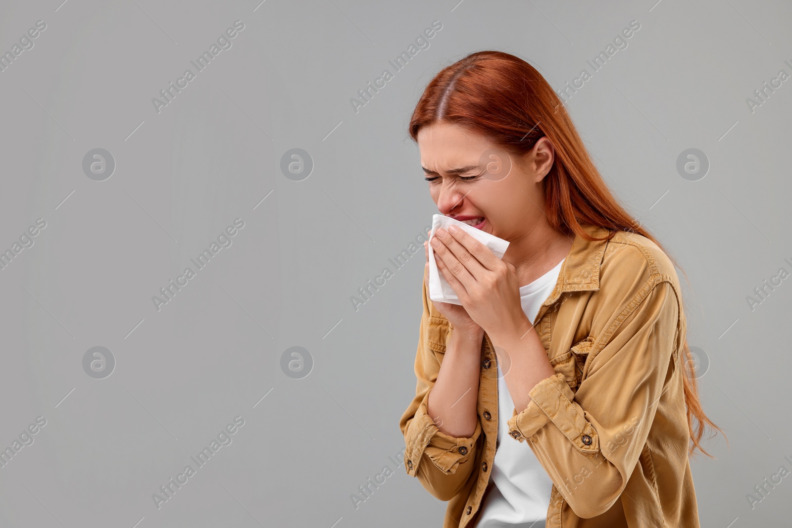 Photo of Suffering from allergy. Young woman with tissue sneezing on grey background, space for text