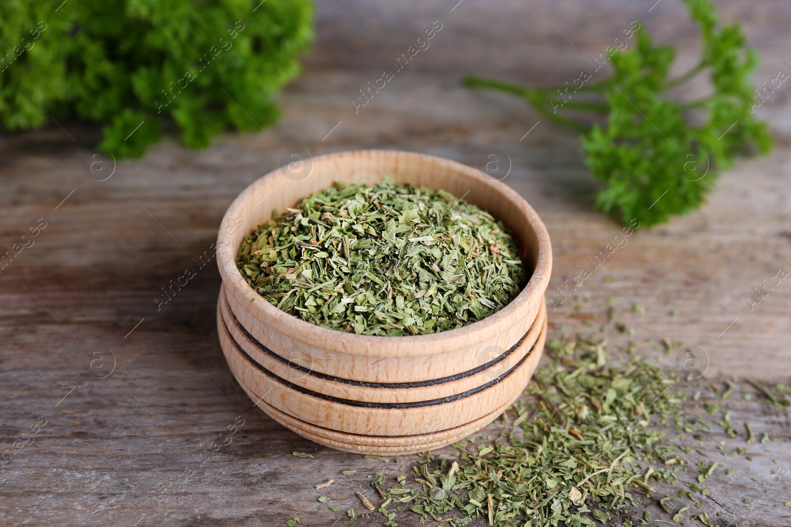 Photo of Bowl with dry parsley on wooden table