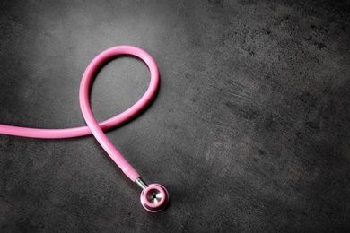 Photo of Pink stethoscope as awareness ribbon on dark background, space for text. Breast cancer concept