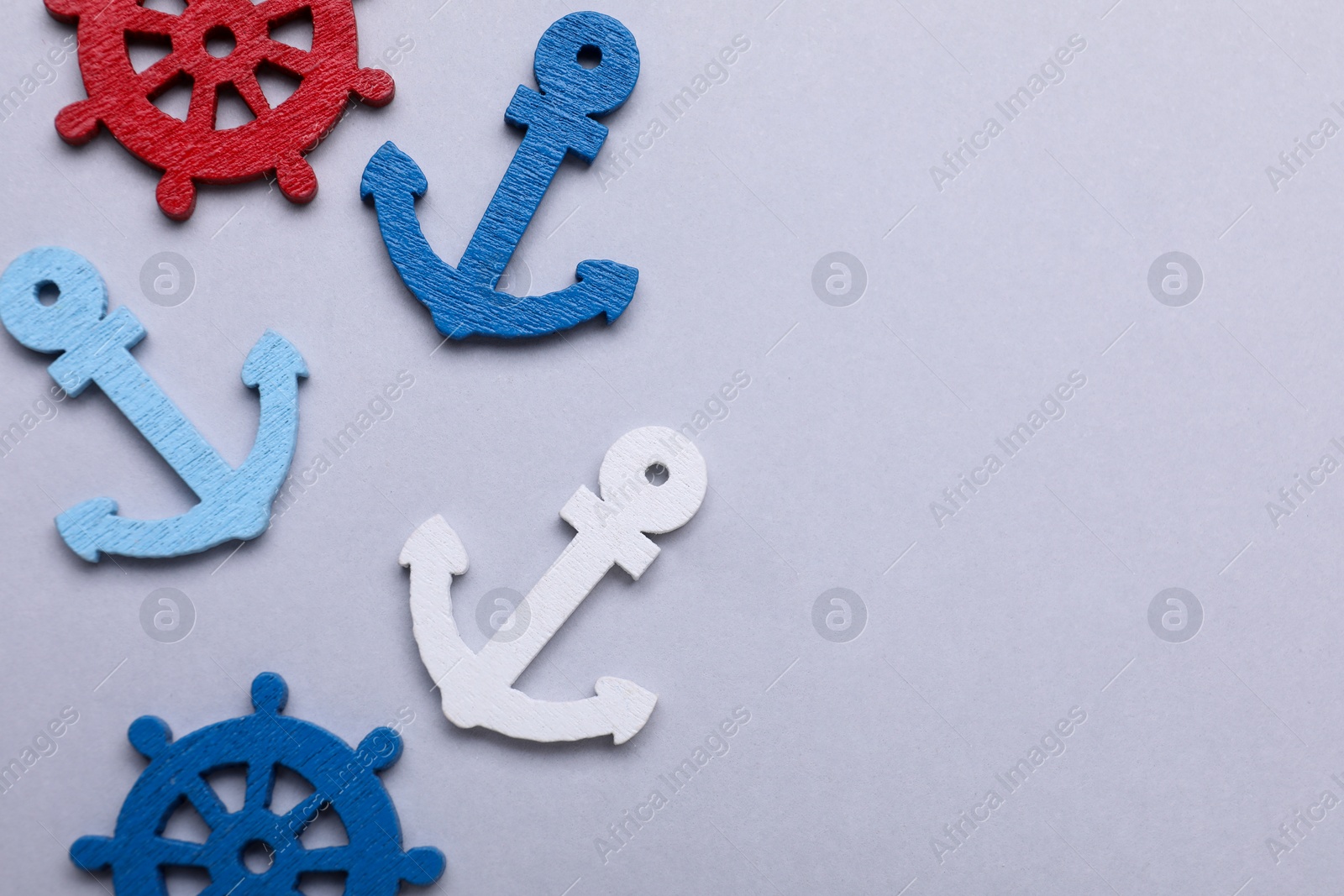 Photo of Anchor and ship wheel figures on light grey background, flat lay. Space for text