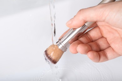 Photo of Woman washing makeup brush under stream of water in sink, closeup