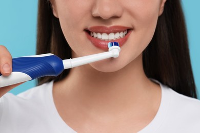 Photo of Woman brushing her teeth with electric toothbrush on light blue background, closeup