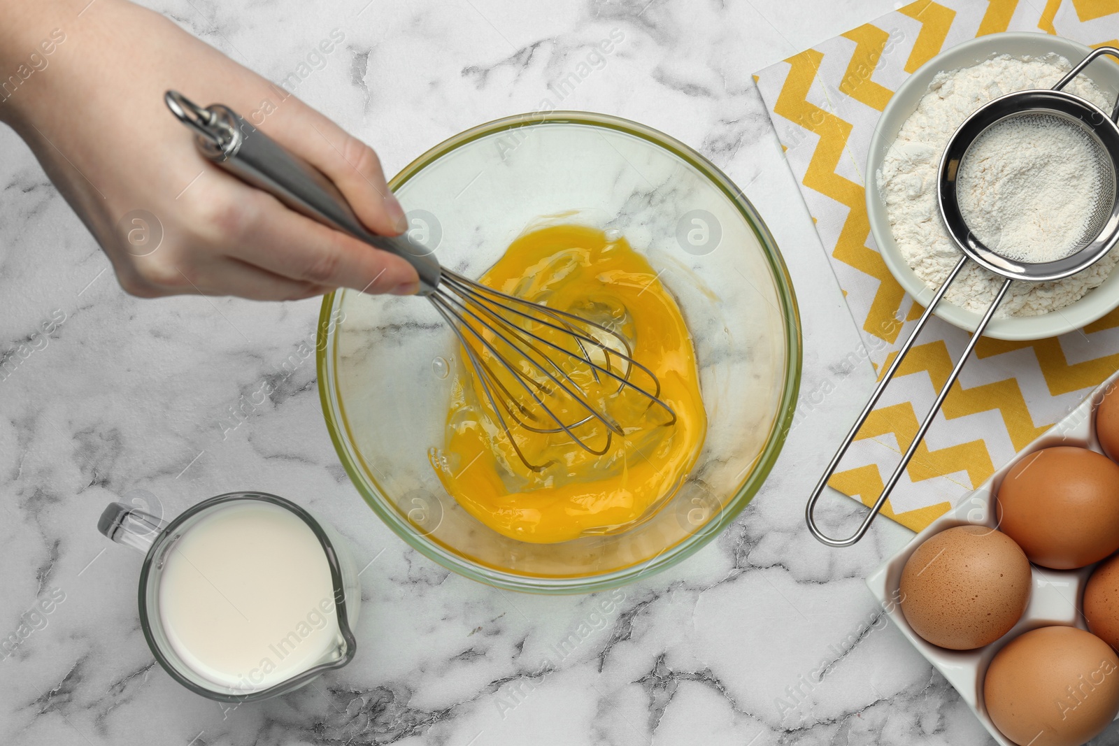 Photo of Woman whisking eggs at white marble table, top view