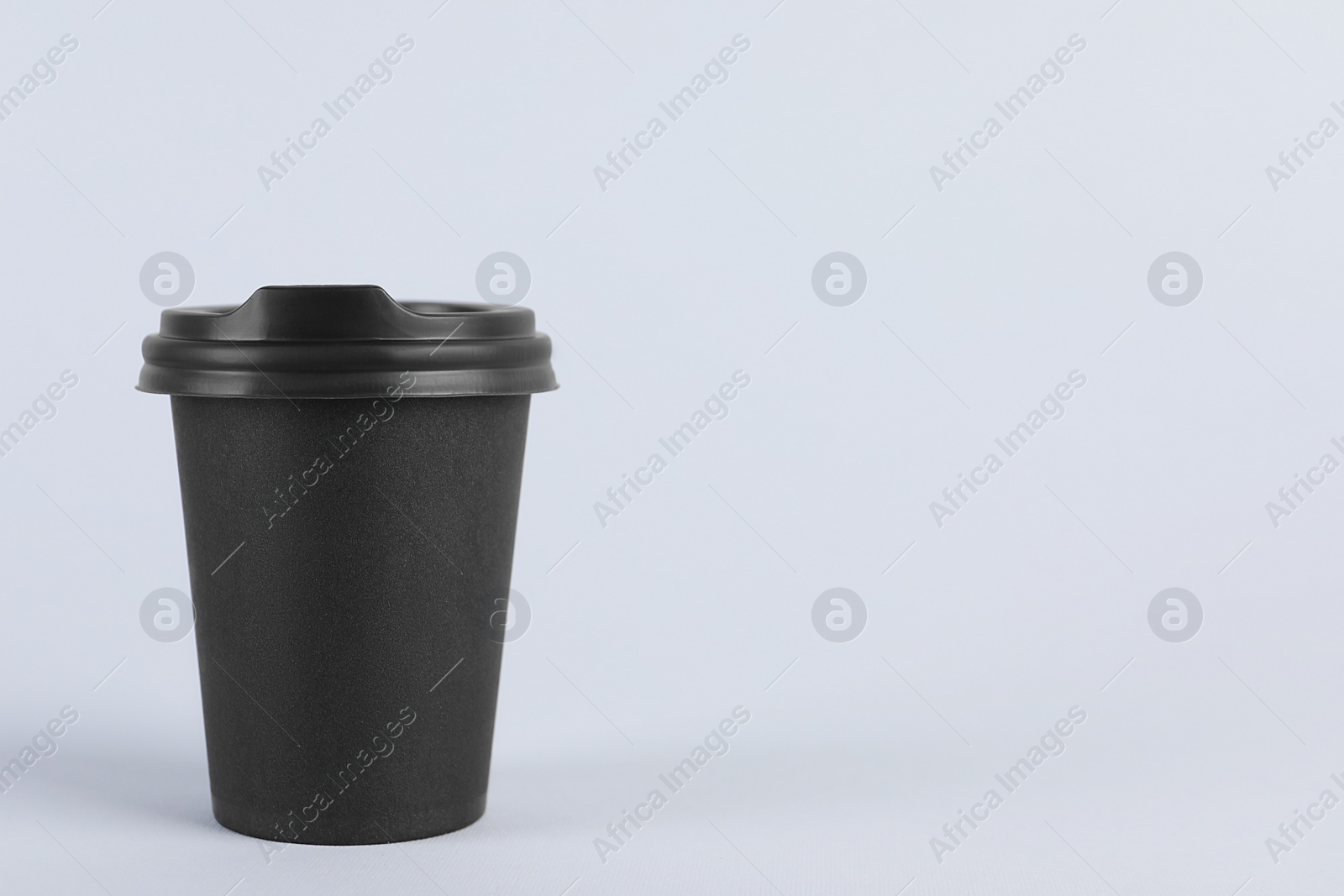 Photo of Black paper cup with plastic lid on light background, space for text. Coffee to go