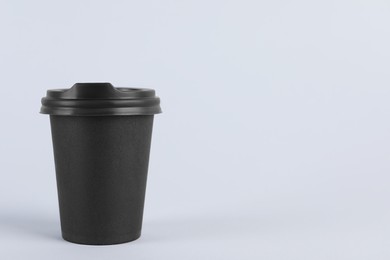 Photo of Black paper cup with plastic lid on light background, space for text. Coffee to go