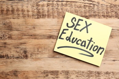 Photo of Note with phrase "SEX EDUCATION" on wooden background, top view. Space for text