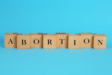 Photo of Word Abortion made of wooden cubes on light blue background