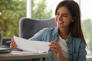 Photo of Young woman reading paper letter at home