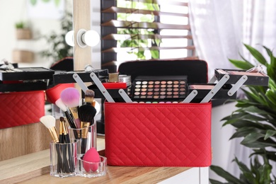 Beautician case with professional makeup products and tools on wooden dressing table