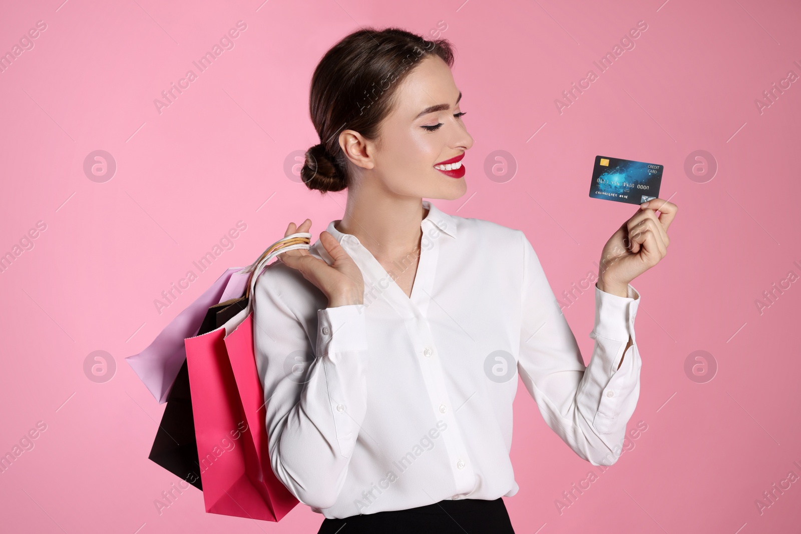 Photo of Happy young woman with shopping bags and credit card on light pink background. Big sale