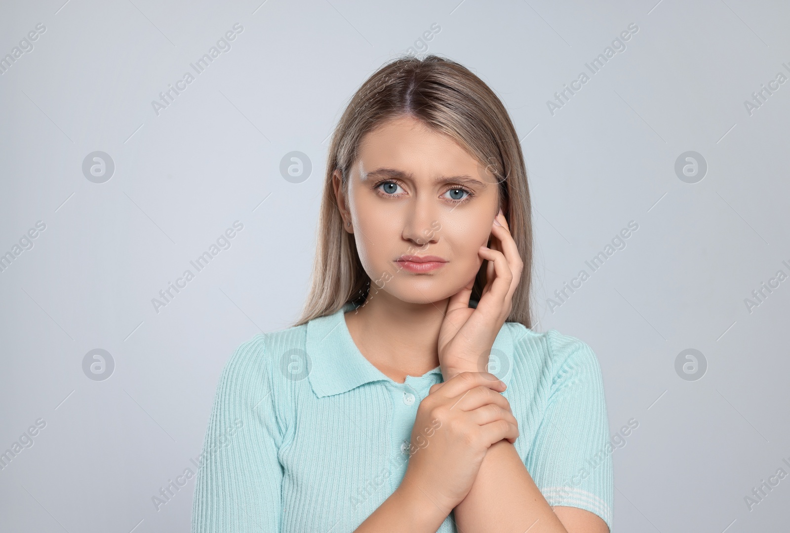 Photo of Young woman suffering from ear pain on light grey background