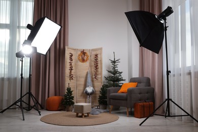 Photo of Beautiful Christmas themed photo zone with professional equipment, trees and armchair in room