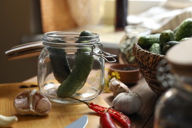 Glass jar with fresh cucumbers and other ingredients on wooden table, closeup. Pickling vegetables