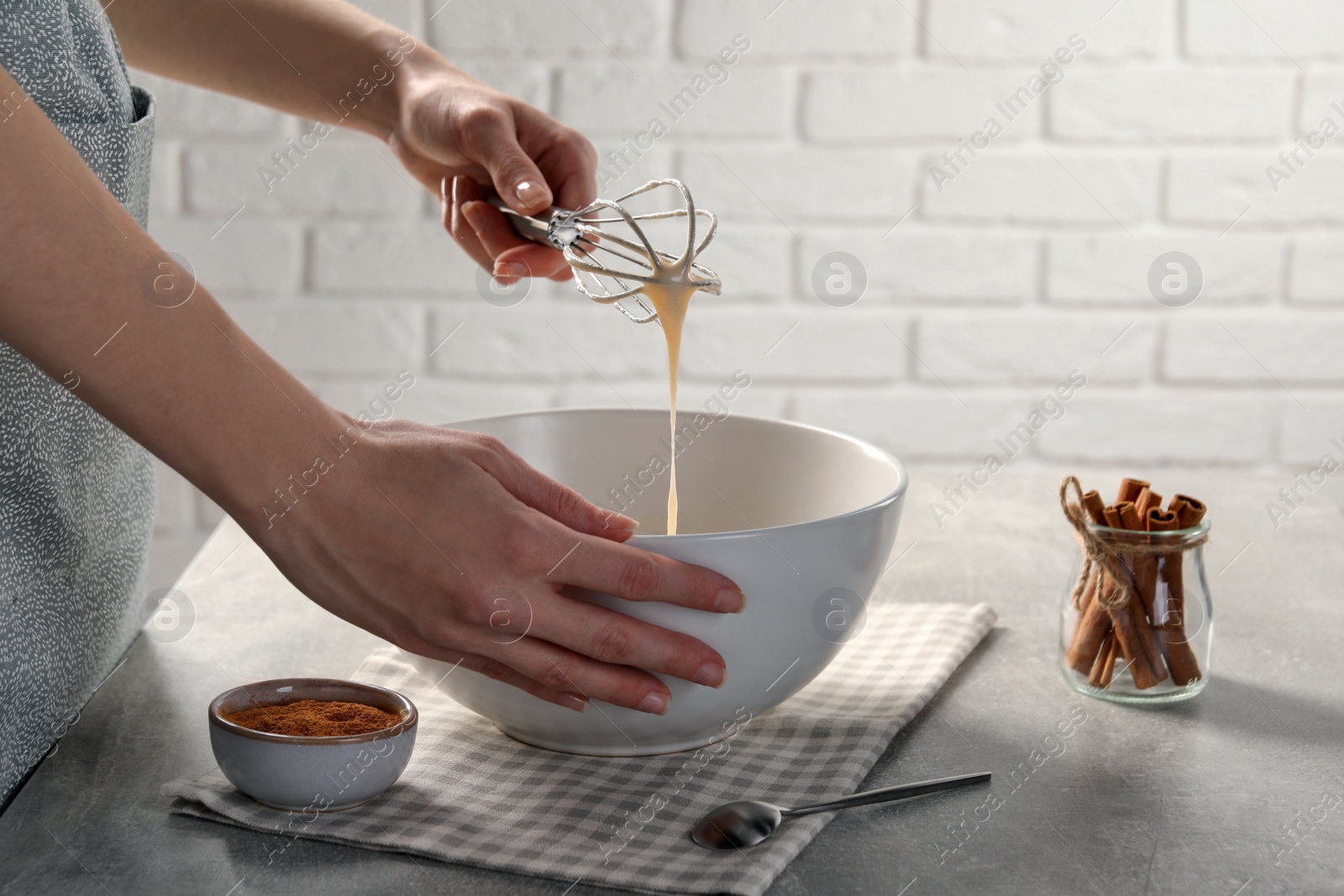 Photo of Woman whipping ingredients with whisk at light grey table, closeup. Cooking delicious eggnog