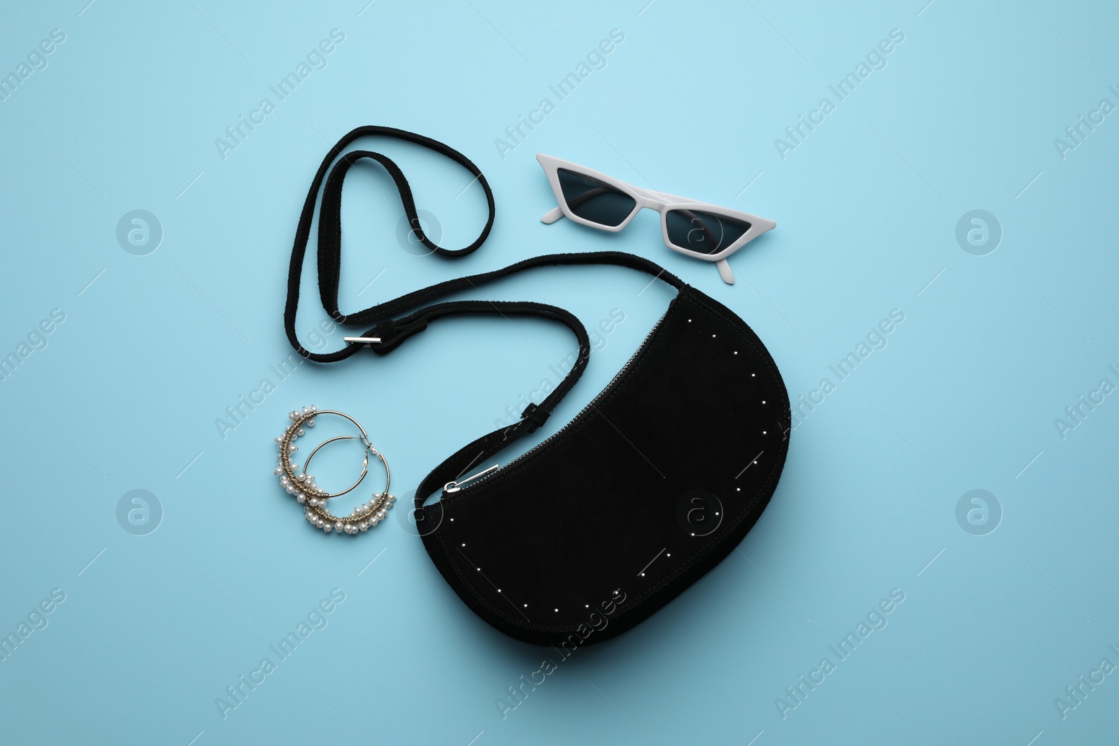 Photo of Stylish woman's bag, sunglasses and earrings on light blue background, flat lay