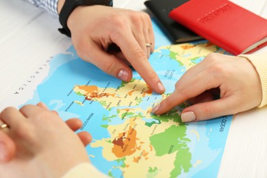 Man and woman planning their honeymoon trip with world map at white wooden table, closeup