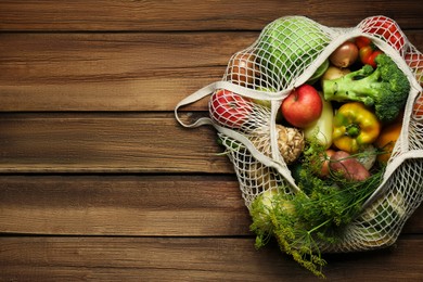 Different fresh vegetables in net bag on wooden table, top view with space for text. Farmer harvesting