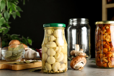 Photo of Glass jars of pickled mushrooms on light grey table