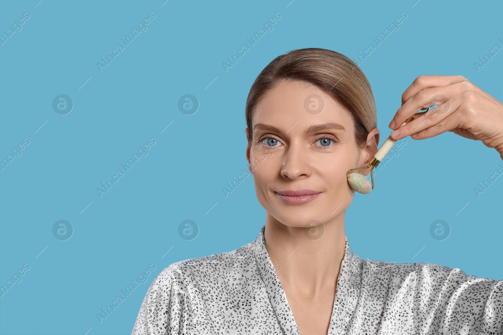 Photo of Woman massaging her face with jade roller on turquoise background. Space for text