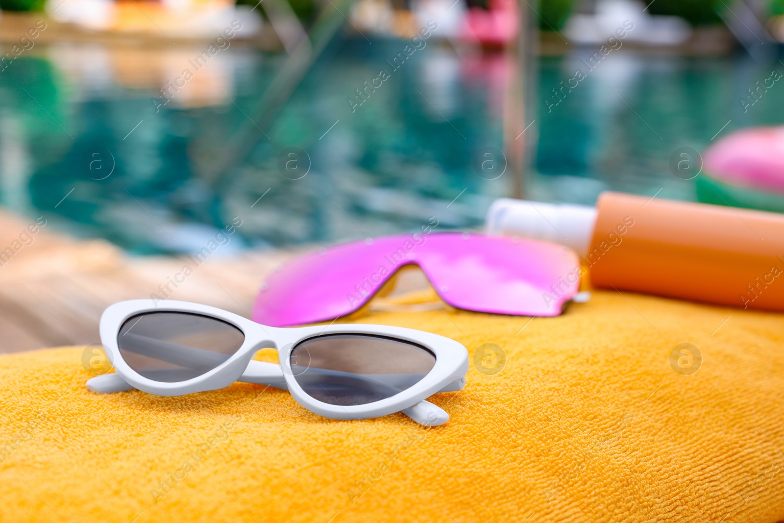 Photo of Sunglasses and sunscreen on beach towel near outdoor swimming pool at luxury resort, closeup. Space for text