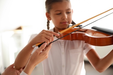 Young woman teaching little girl to play violin indoors, focus on hands