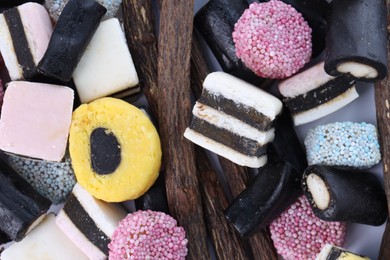 Many tasty candies and dried sticks of liquorice root on white background, flat lay