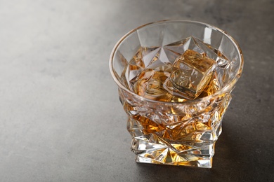 Photo of Golden whiskey in glass with ice cubes on table. Space for text