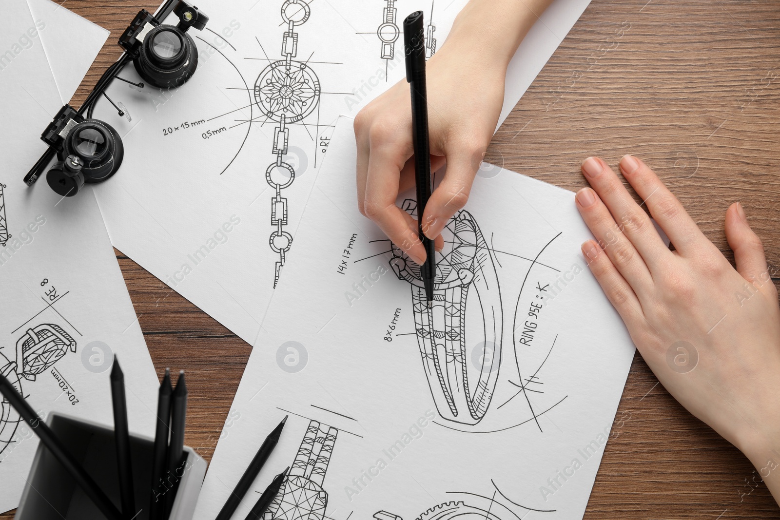 Photo of Jeweler drawing sketch of elegant ring on paper at wooden table, top view