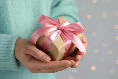 Photo of Woman holding gift box with pink bow against blurred festive lights, closeup and space for text. Bokeh effect