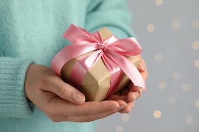 Woman holding gift box with pink bow against blurred festive lights, closeup and space for text. Bokeh effect