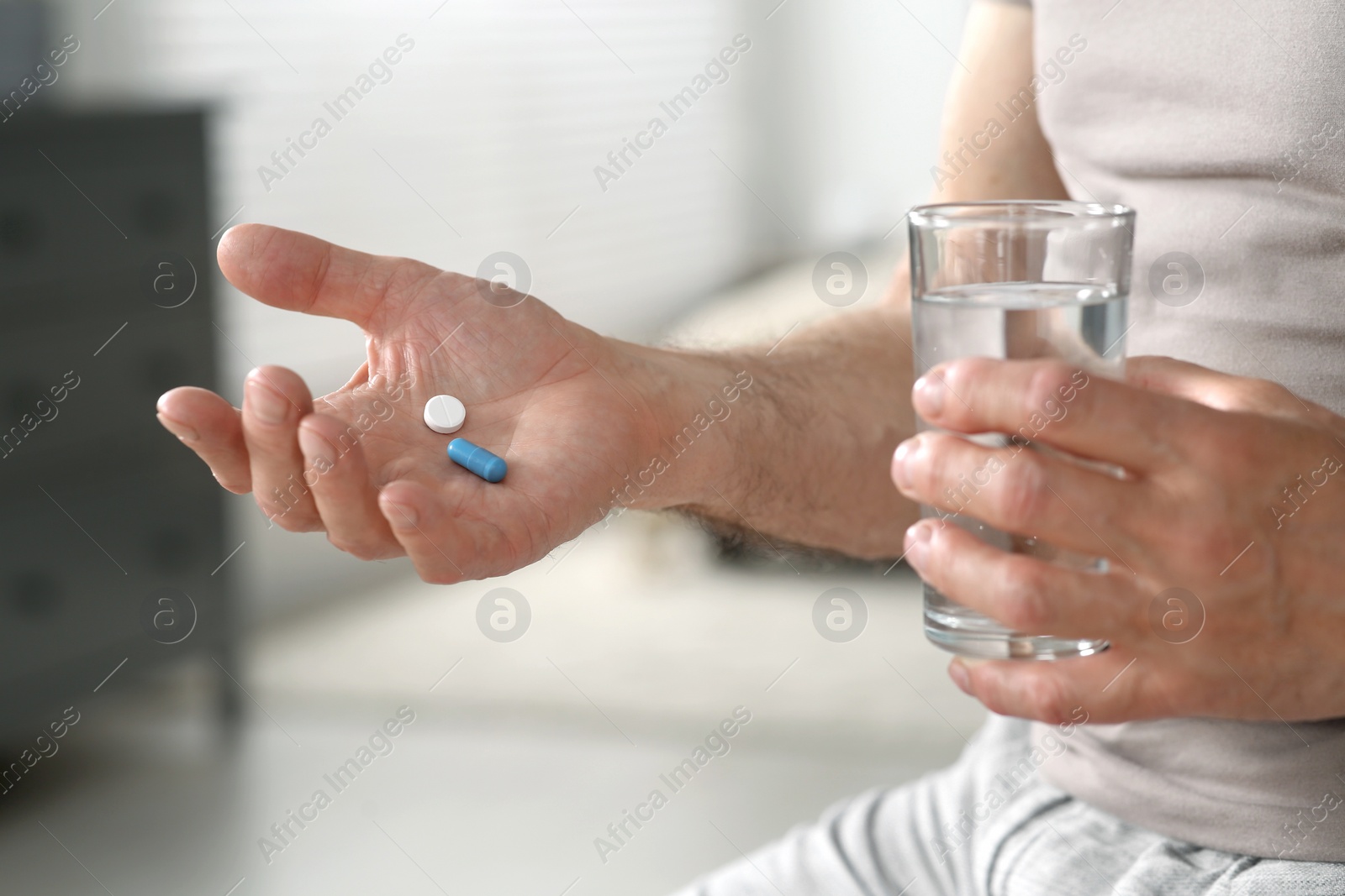 Photo of Senior man with pills and glass of water indoors, closeup