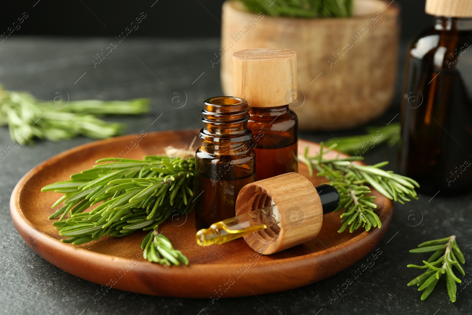 Photo of Essential oils in bottles and rosemary on gray table, closeup