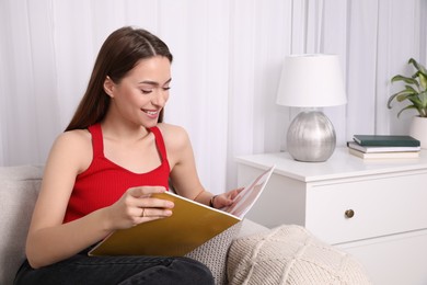 Photo of Young woman reading fashion magazine at home