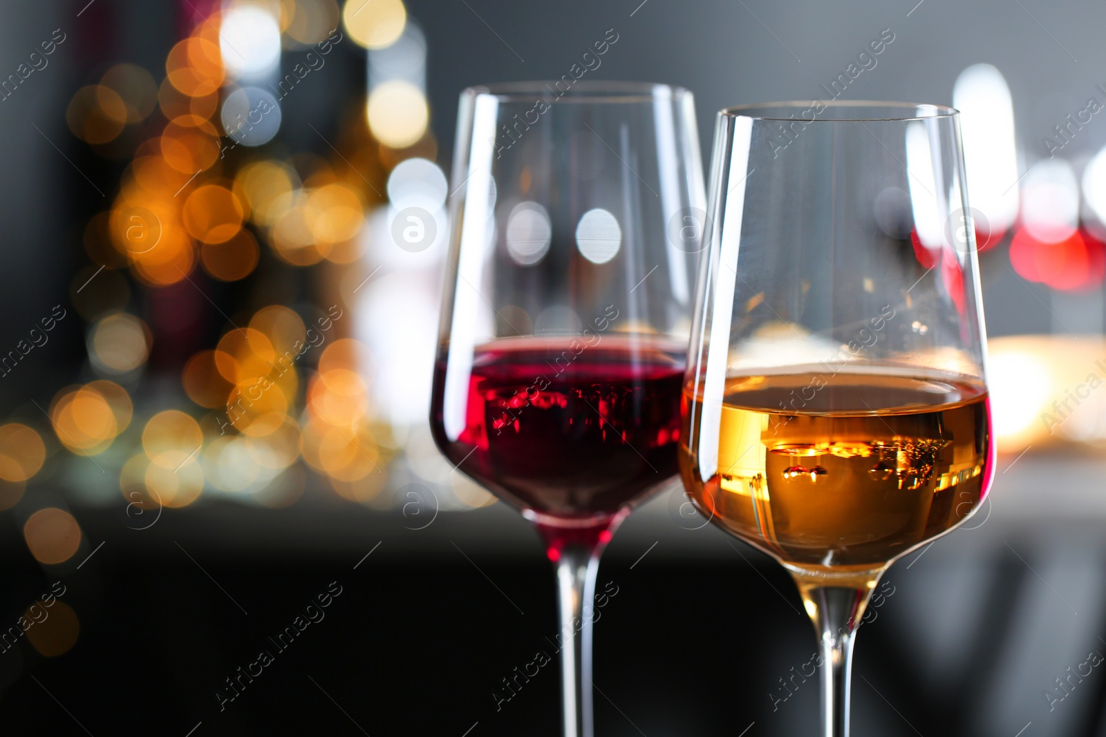 Photo of Glasses with different wines against defocused lights, closeup. Space for text