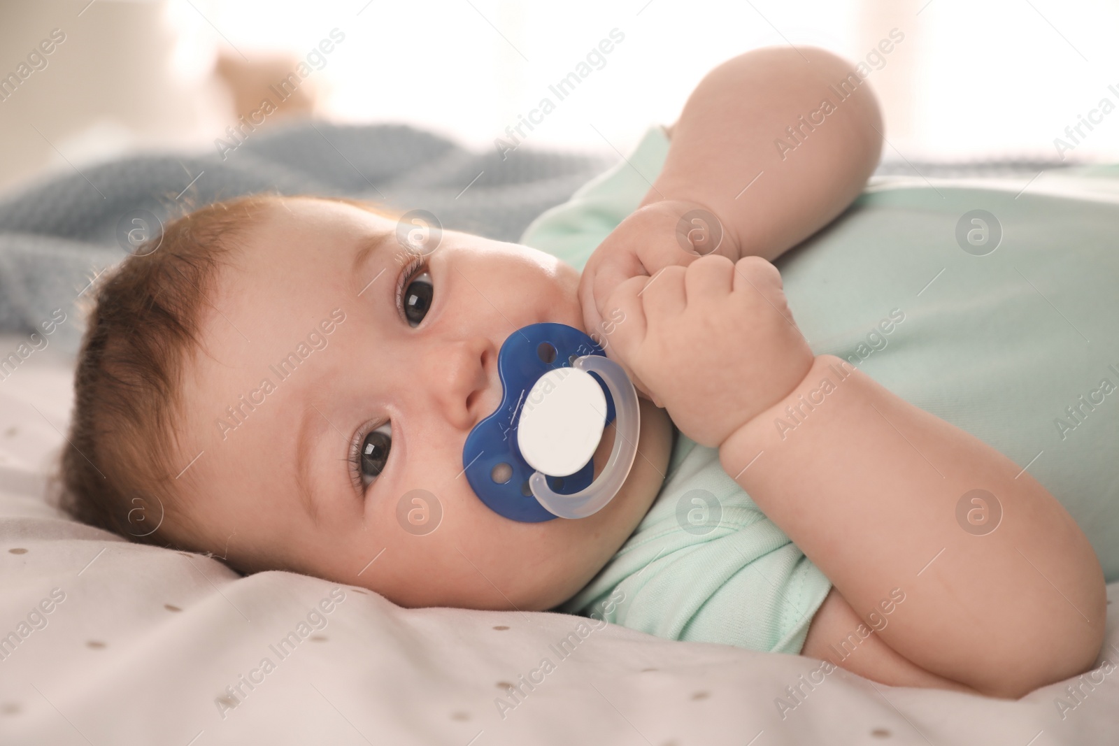 Photo of Cute little baby with pacifier on bed at home