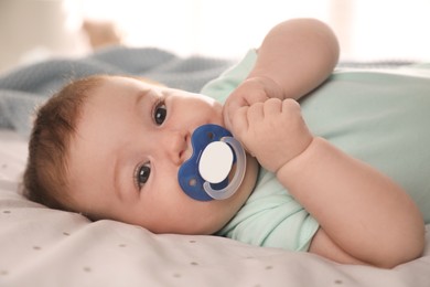 Photo of Cute little baby with pacifier on bed at home